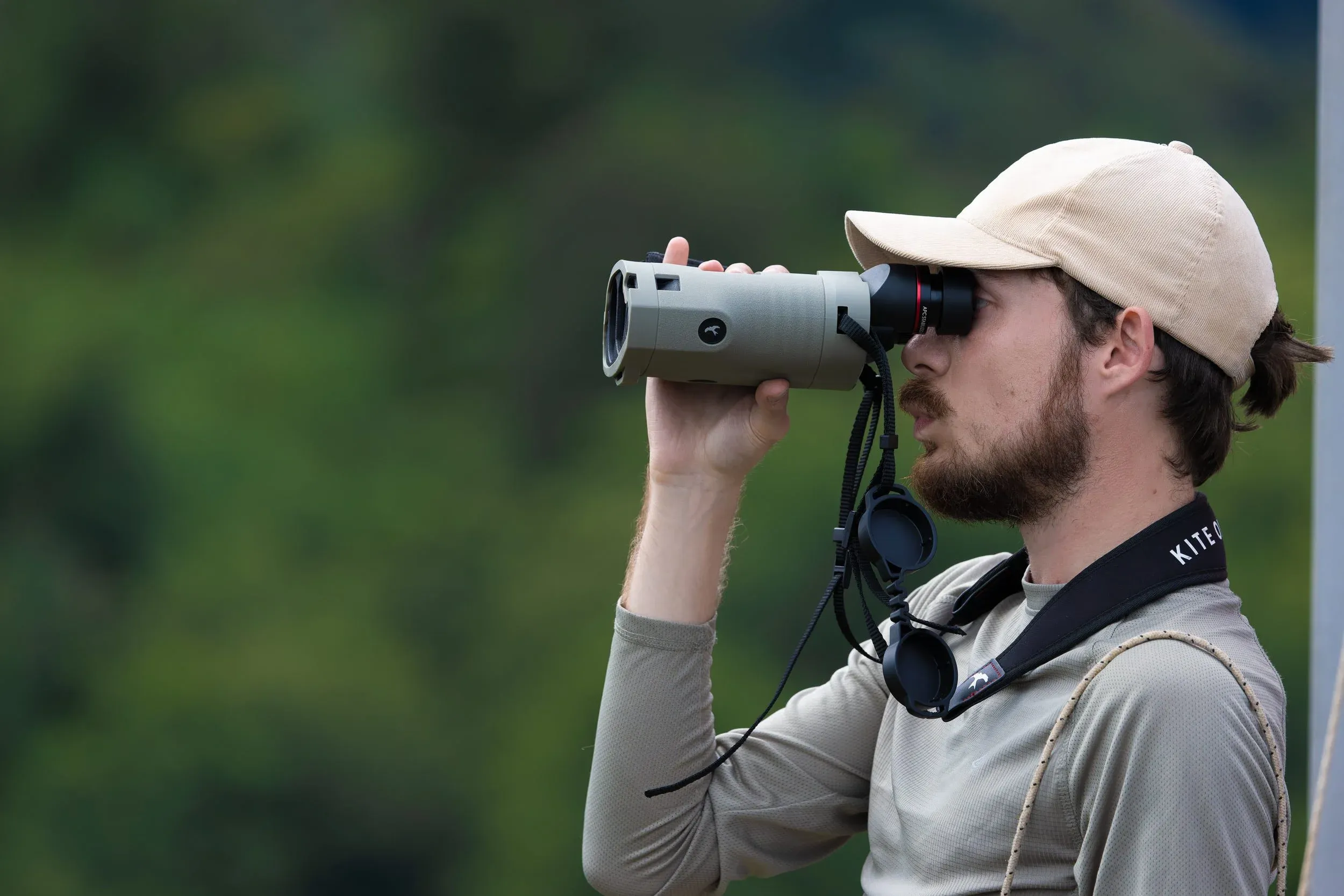 A counter scanning the sky with Kite Optics binoculars, green hills behind